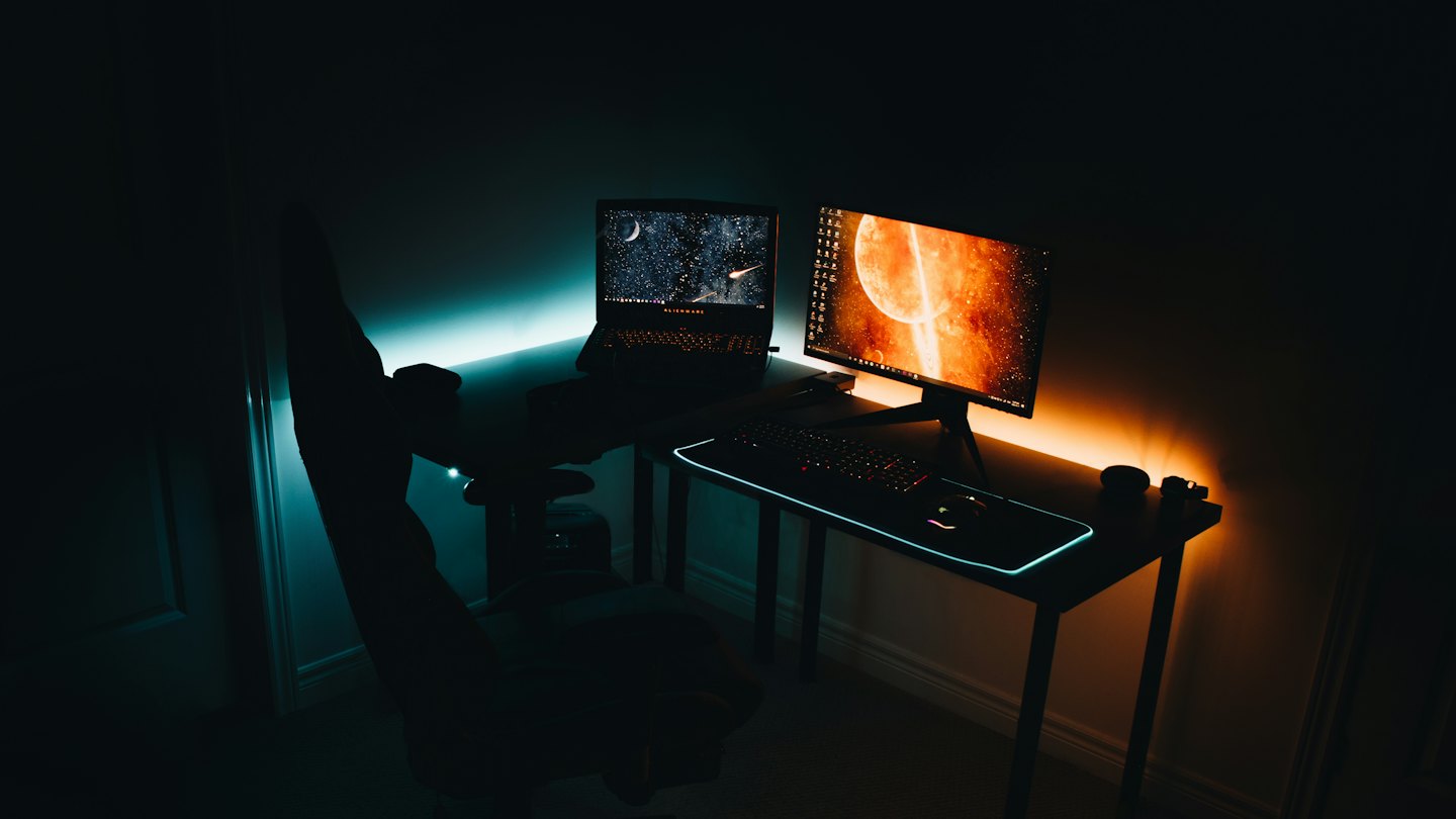 Bureau de jeu avec ordinateur portable, écran et lumières LED colorées.